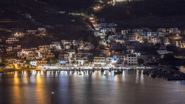 Amorgos island aerial night timelapse from above. Traditional Greece - illuminated white houses on hills and sea port in harbor, Cyclades