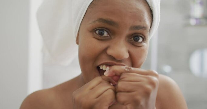 Happy african american woman flossing teeth and using smartphone in bathroom
