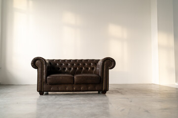 Leather sofa in baroque style against a white wall with sunlight. Shadows on the wall