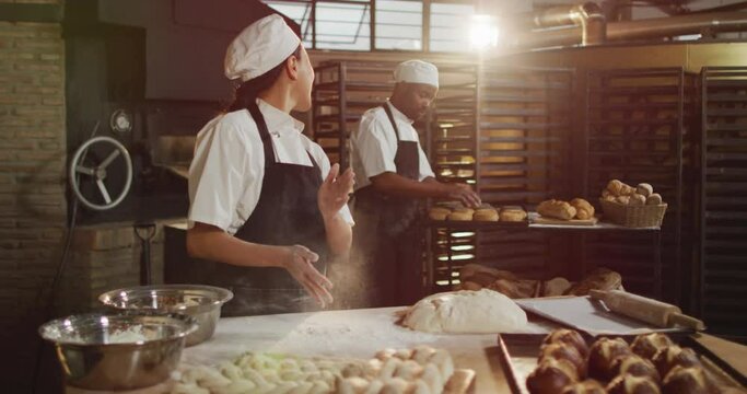 Animation of happy asian female baker cleaning hands from flour and talking with male coworker