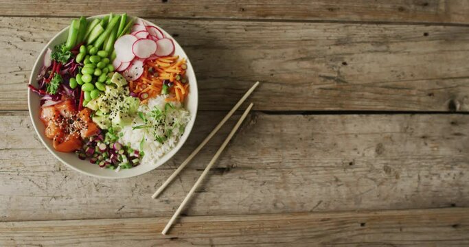 Composition of bowl of rice, salmon and vegetables with chopsticks on wooden background