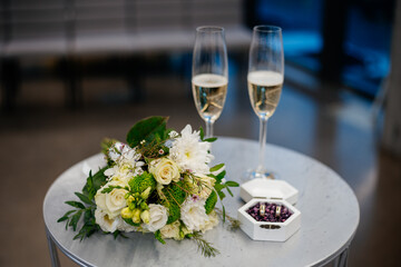 Before the wedding ceremony at the registry office decoration composition: wedding rings for the bride and groom in a box on the table next to the wedding bouquet and two glasses of champagne