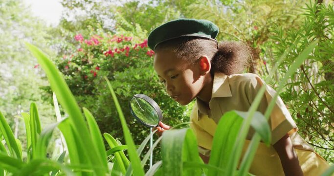 Animation of african american girl in scout costume using magnifier in garden