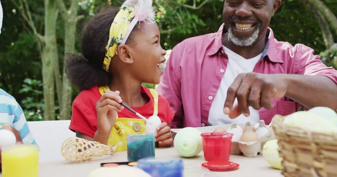 Animation of happy african american grandfather and grandchildren painting easter eggs in garden