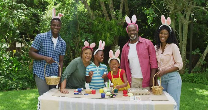 Animation of happy african american family wearing bunny ears and posing to photo in garden