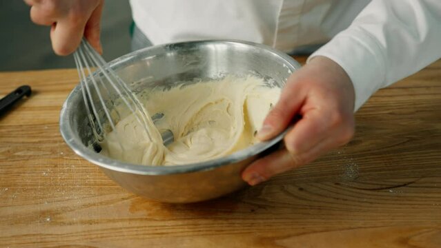 Professional kitchen: the male chef is mixing pancake in the bowl by using the whisk