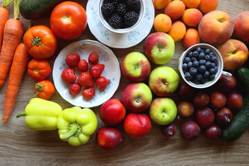 Berries in vintage porcelain dishes, other healthy fruit and vegetable on wooden table. Top view.