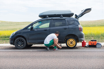 A man changes a wheel on a car on the side of the road.Concept:replacement of wheels in a car, a...