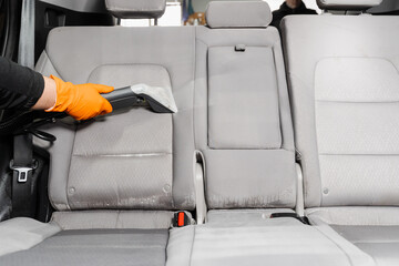 Cleaning textile seats in car interior using extractor machine for dry clean. Car cleaner is...