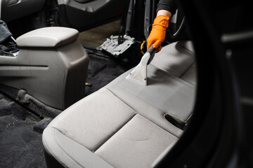 Cleaning textile seats in car interior using extractor machine for dry clean. Car cleaner is...