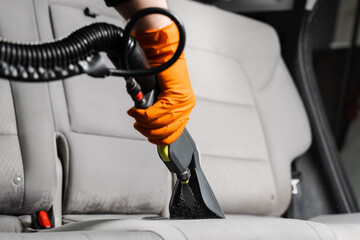Close-up dry cleaning extractor machine is spraying water and detergent on textile seat inside car. Car dry cleaner is using extraction machine for removing stains and dirt from textile seats.