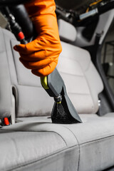 Close-up dry cleaning extractor machine is spraying water and detergent on textile seat inside car....