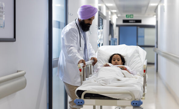 Sikh male doctor in turban with girl lying on hospital bed