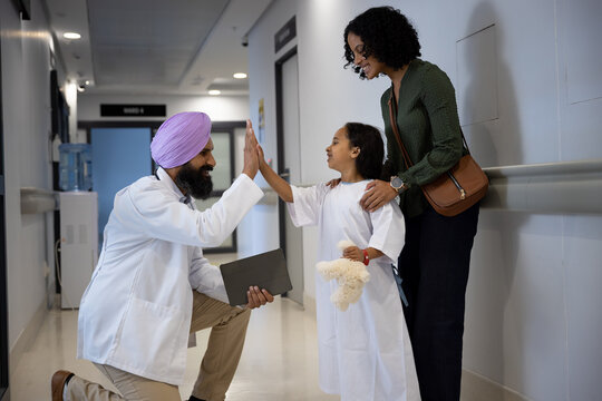 Sikh male doctor in turban high fiving with daughter and mother embracing in hospital