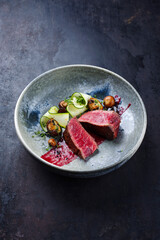 Fried Italian chianina beef fillet steak very rare with mushrooms, zucchini and amarena sauce served as close-up in a Nordic design bowl