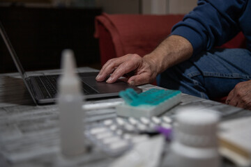 Close-up of a senior's hand using a laptop with medication beside it