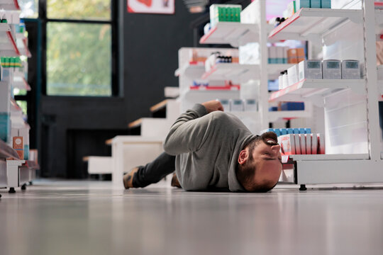 Unconscious person lying on pharmacy floor during epileptic attack, suffering from epilepsy disorder. Drugstore young client fainting, having seizure with foaming at mouth