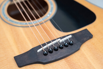 detail of the bridge of a light wood acoustic guitar with its pegs and pins, selective focus, horizontal