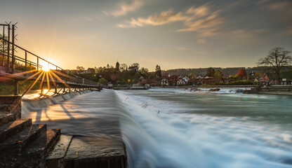 Schäumendes Wasser beim Streichwehr/Flusstufe in der Reuss bei Unterwindisch. Die Abendsonne scheint durch die Wehrbrücke.
