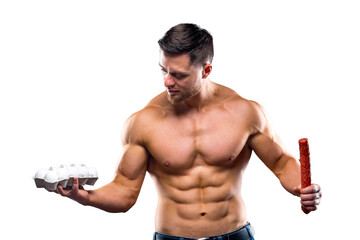 Bodybuilder sportsman holding eggs and sausage . Choosing between healthy and harmful food. naked...
