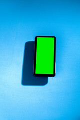 Mobile phone with green screen on top of a blue table. smartphone concept. Green screen concept.