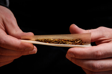 Hands close up rolling a Joint full of hashish, marijuana cannabis extract. Drugs narcotic concept