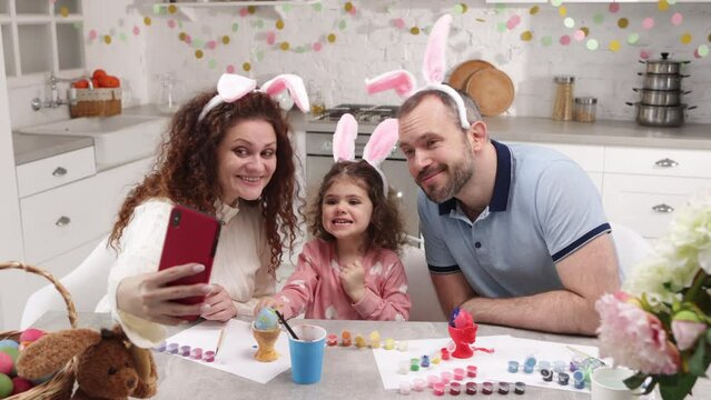 Portrait of caucasian family with little, cute daughter wearing bunny ears and taking pictures. Loving parents creating memories while celebrating Easter holidays. High quality 4k footage