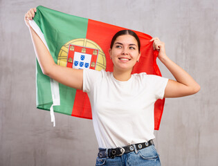 Joyful girl stands with flag of Portugal in her hands. Isolated on gray background