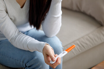 A sad woman holds a pregnancy test in her hand. Unwanted pregnancy concept. - obrazy, fototapety, plakaty