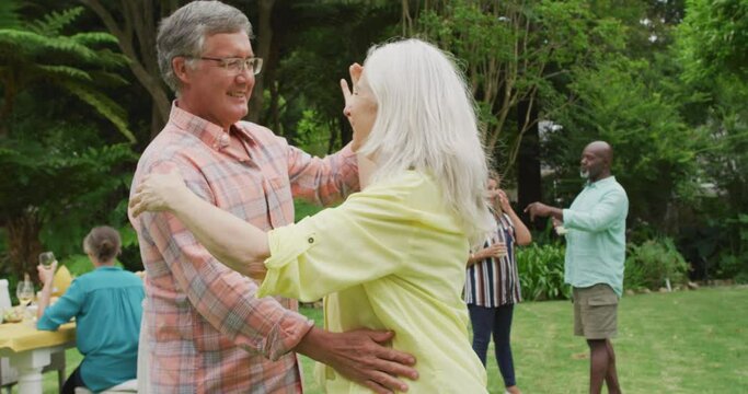 Animation of happy caucasian senior couple danging in garden while having lunch with friends