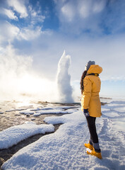 A girl standing in front of Famous Geysir in Iceland in beautiful sunrise light. One of the most...