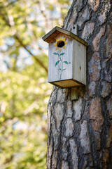 A bird feeder in the form of a house with a wooden roof hangs on a tree. Bird care. Wooden house close-up with copyspace