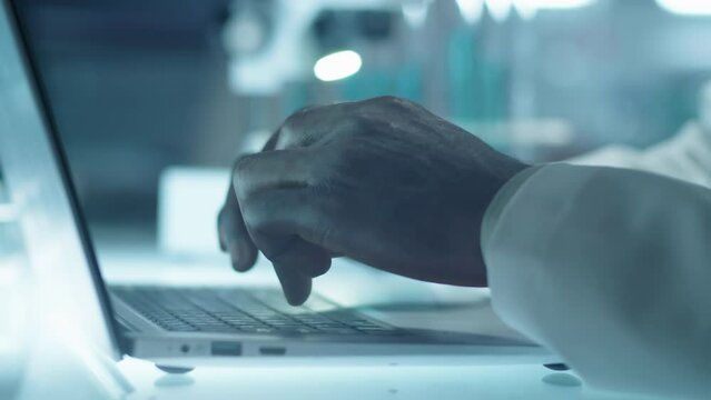 Close up shot of hands of male laboratory scientist typing on laptop keyboard at workplace