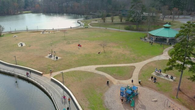 Aerial footage of people playing and walking in the park with rippling waters on the lake and lush green trees and yellow winter grass at Rhodes Jordan Park in Lawrenceville Georgia USA