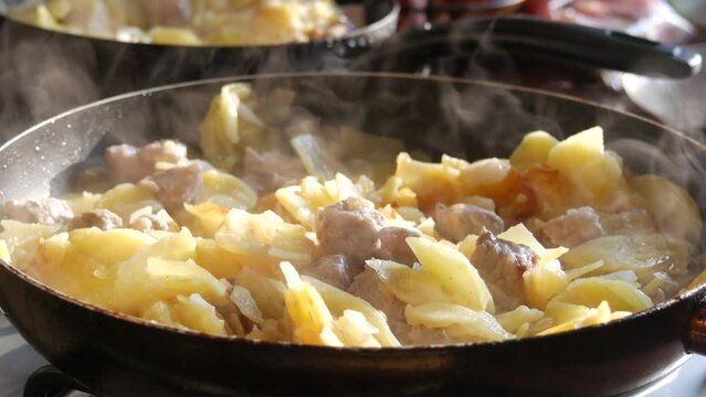Fried potatoes in a pan with spices and pieces of meat in a home kitchen. Steam over hot food