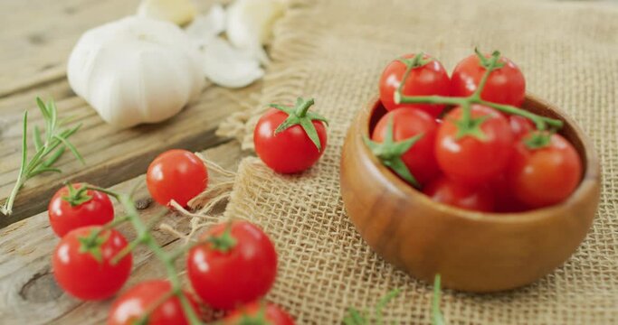 Video of fresh cherry tomatoes in bowl and garlic on rustic cloth over wooden background