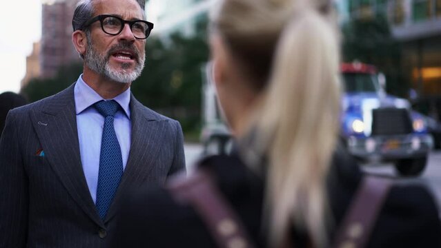 Adult Prosperous businessman in suit and stylish eye glasses stands on city street while talking to female colleague. Business people discussing something while standing on busy street. Communication
