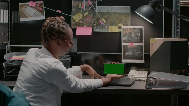 Young inspector using greenscreen in archive office space, examining chroma key display and conducting investigation. Detective checking isolated mockup template with copyspace.