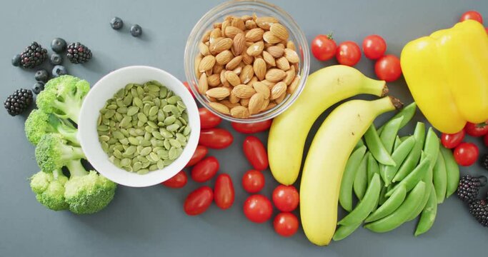Video of fresh fruit and vegetables and bowls of nuts and seeds over grey background