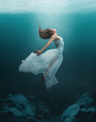 Underwater dancer in an artistic elegant pose with natural lighting from ocean surface