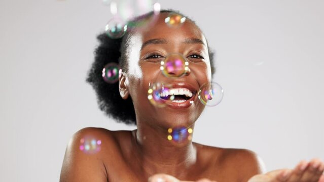 Face, skincare and water splash of happy black woman in studio isolated on a gray background. Cleaning portrait, cosmetics bubbles and laughing female model apply lotion, cream or skin moisturizer.