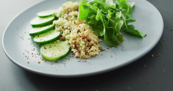 Video of fresh sliced cucumber, leaves and grains salad on grey plate over dark grey background
