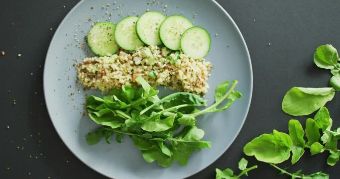 Video of fresh sliced cucumber, leaves and grains salad on grey plate over dark grey background