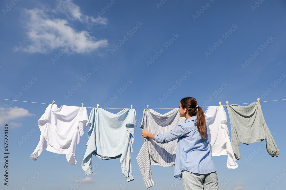 Wall mural Woman hanging clothes with clothespins on washing line for drying against cloudy sky outdoors