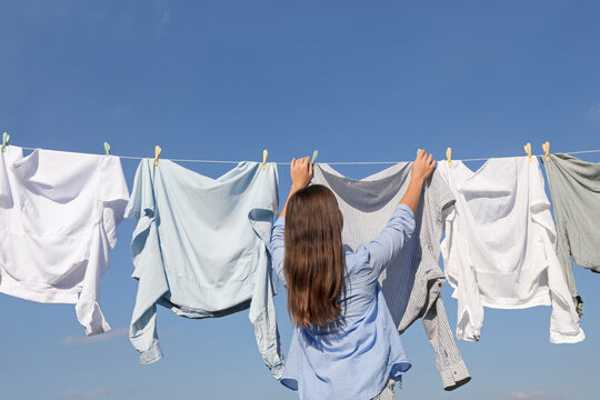 Woman hanging clothes with clothespins on washing line for drying against blue sky, back view