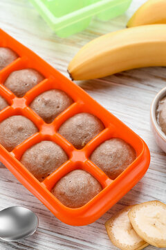 Banana puree in ice cube tray with ingredients on white wooden table