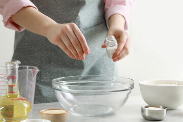Woman adding pinch of salt into bowl at grey marble table indoors, closeup. Cooking traditional...