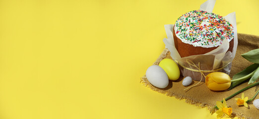 Traditional Easter cake with sprinkles, decorated eggs and flowers on yellow background, space for text. Banner design