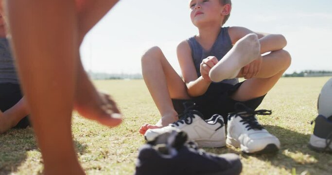 Video of happy diverse boys sitting on lawn and taking off socks