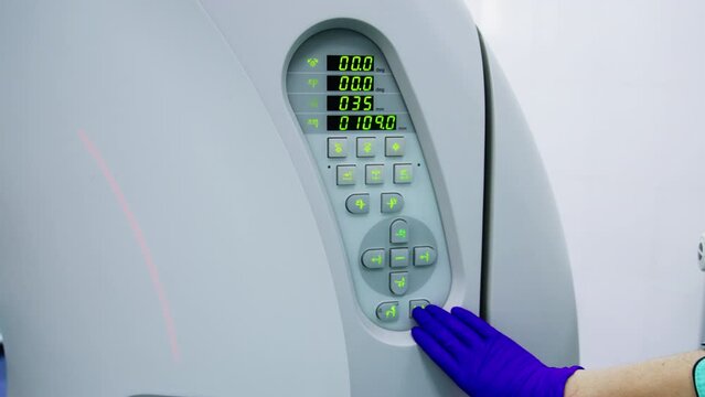 Gloved hand of medic setting the parameters on modern tomography scanner. Patient having a check up at the innovative equipment. Close up.